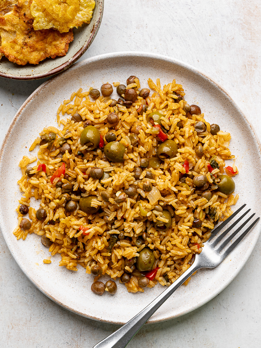 Arroz con gandules served on a white plate with tostones on the side. 