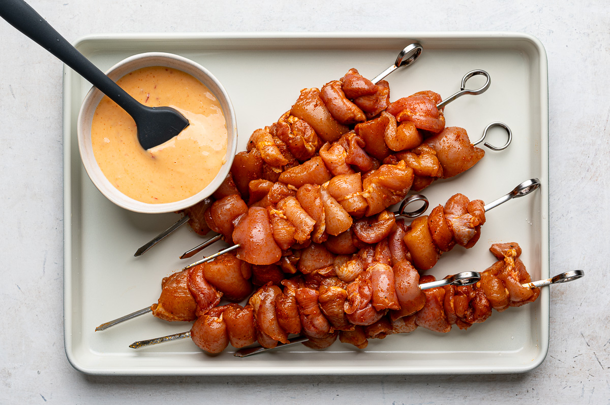 Seasoned chicken pieces threaded through metal skewers with bang bang sauce on the side. 