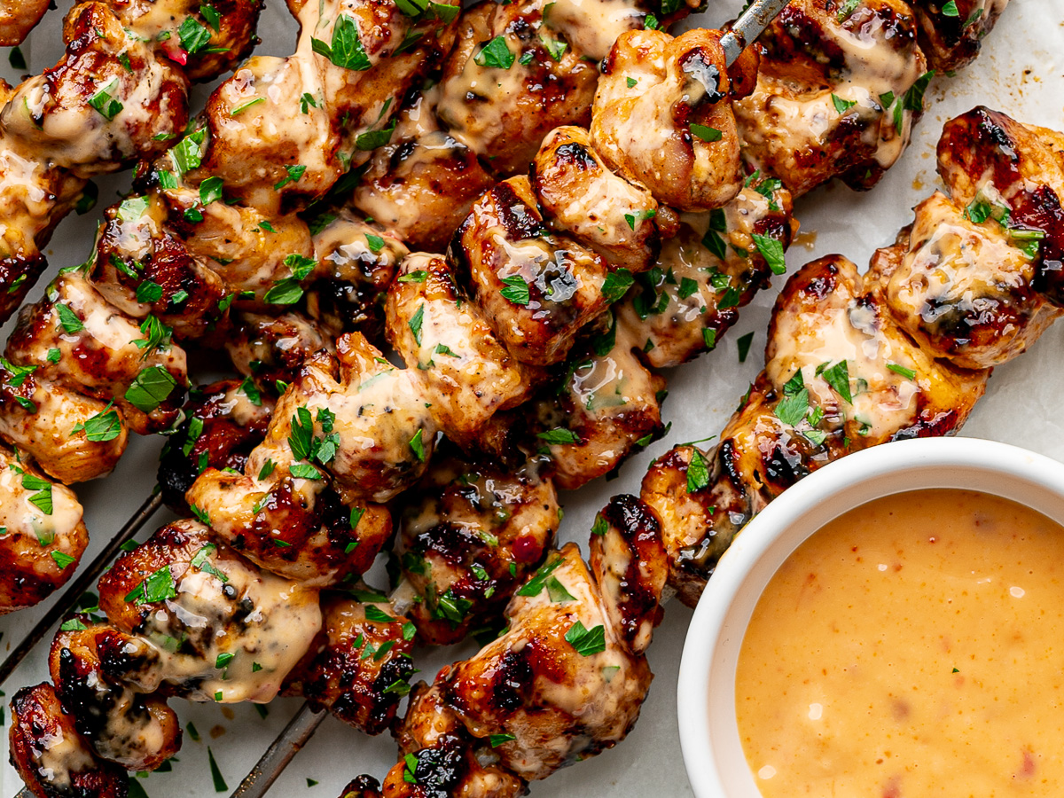 Close-up of grilled chicken skewers brushed with bang bang sauce with extra sauce on the side.