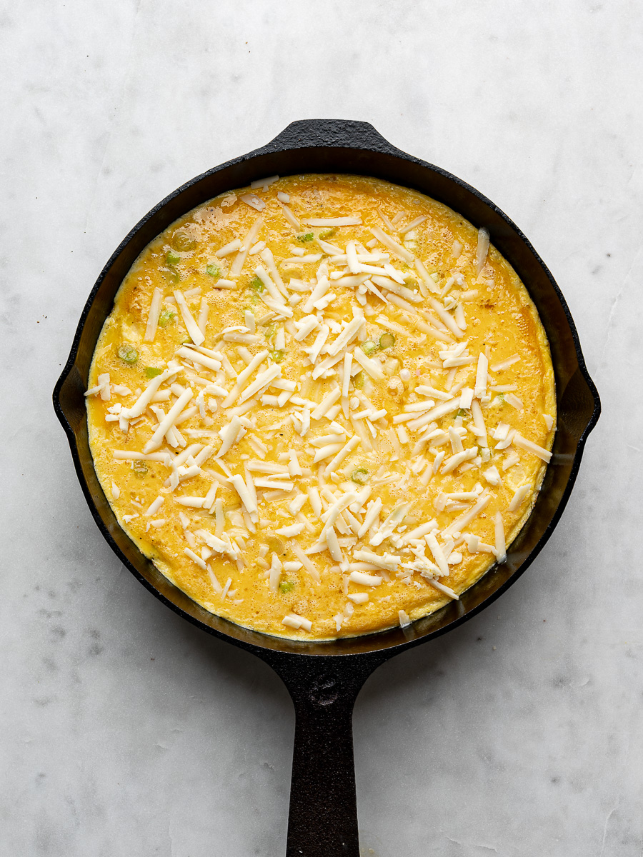 Un-baked frittata in cast iron skillet topped with grated cheese. 