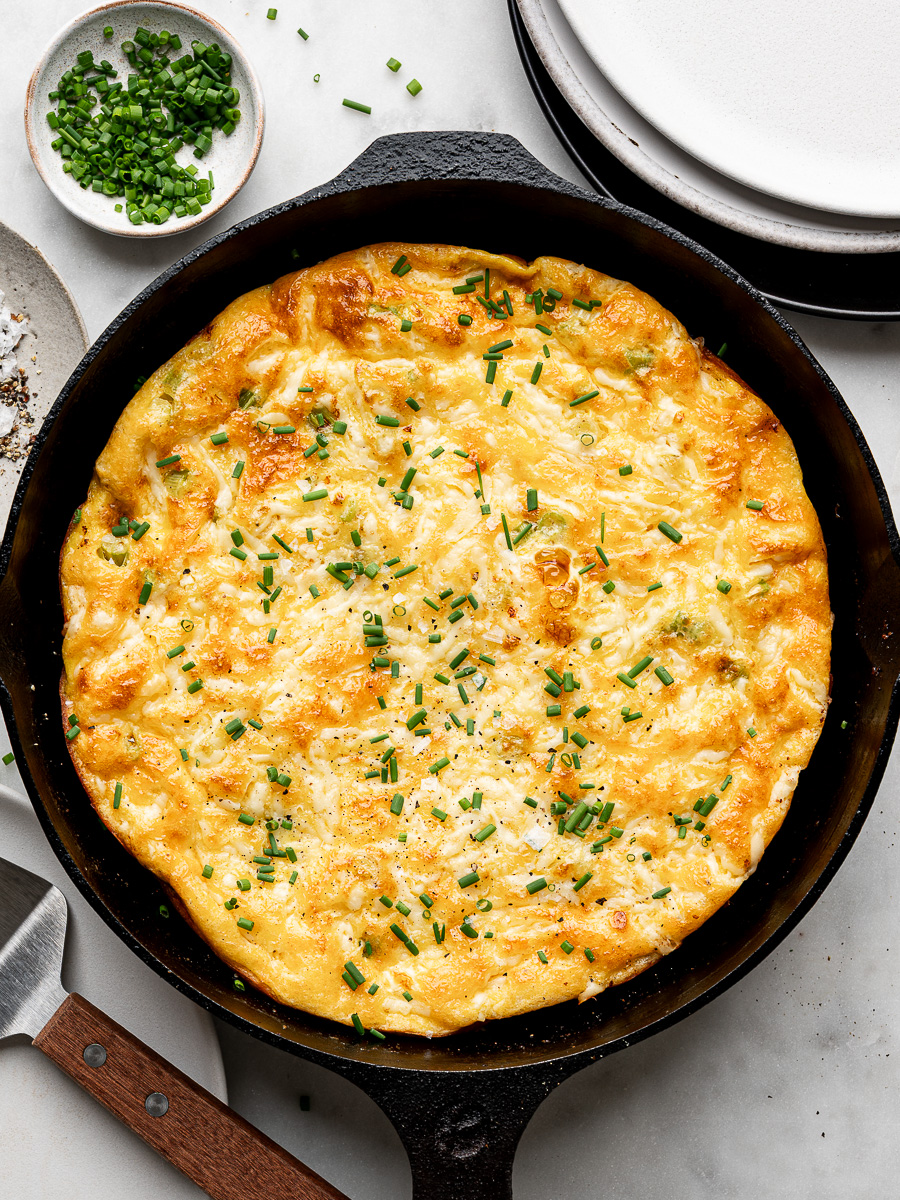Closeup of cheesy ham and onion frittata garnished with chopped chives. 