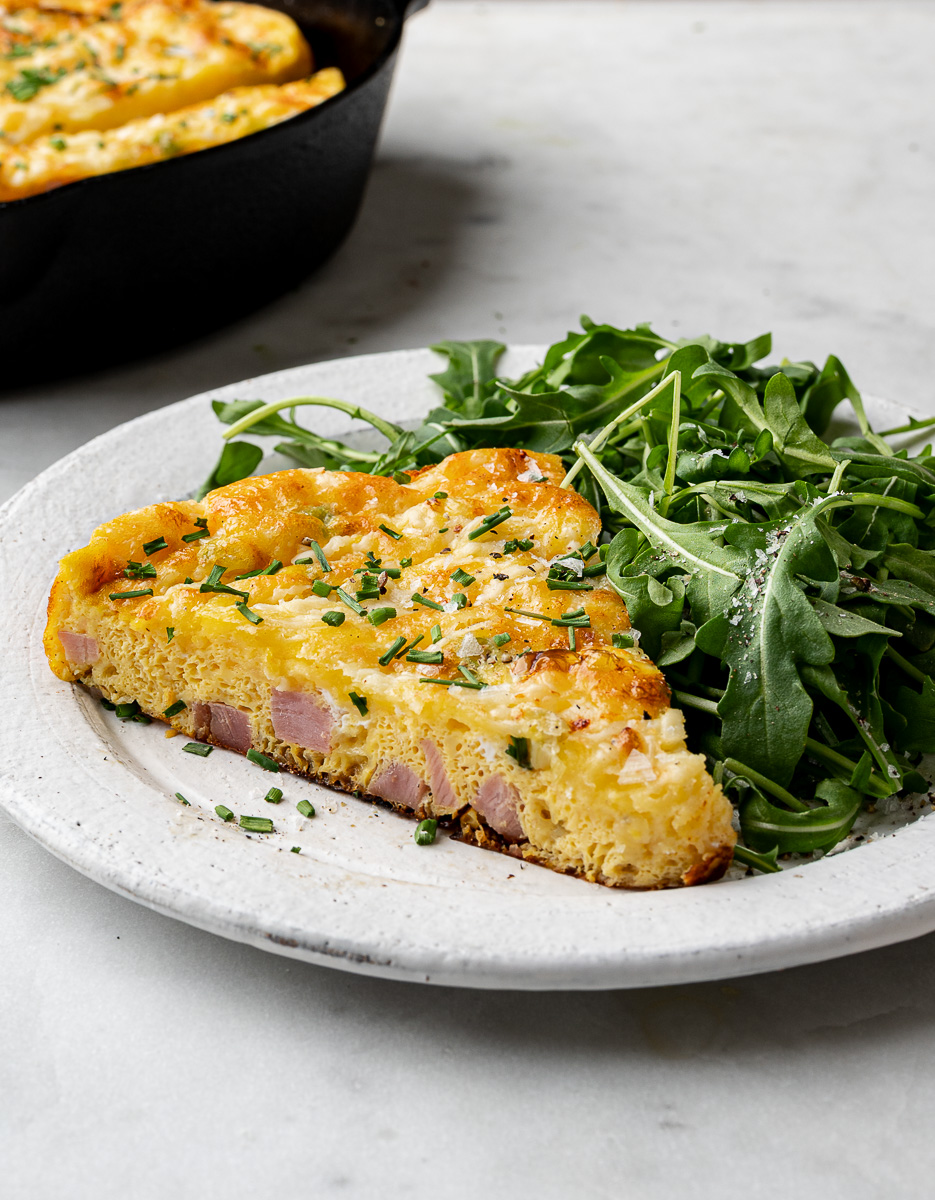 Oven-baked ham and cheese frittata sliced and served on a plate with fresh salad. 