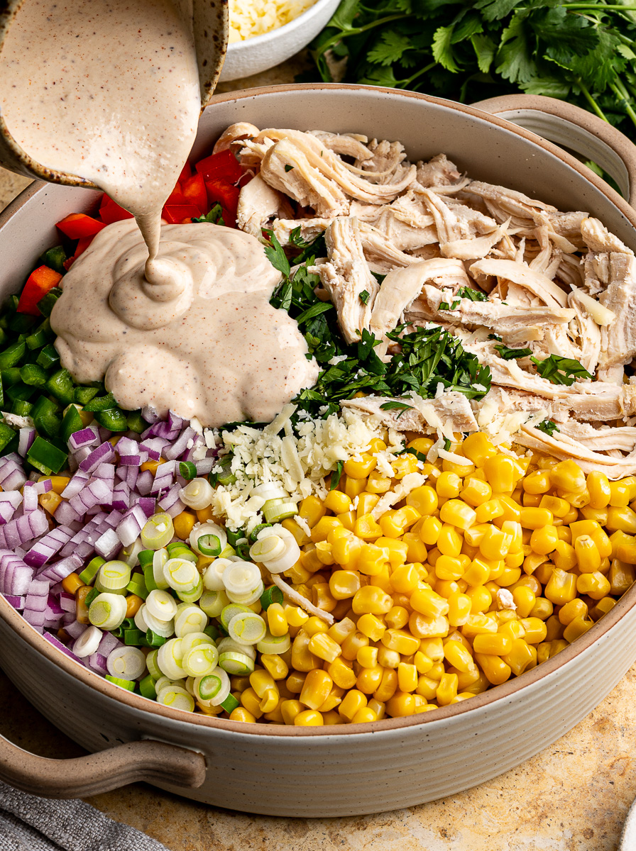 Pouring dressing over top of chicken salad. 