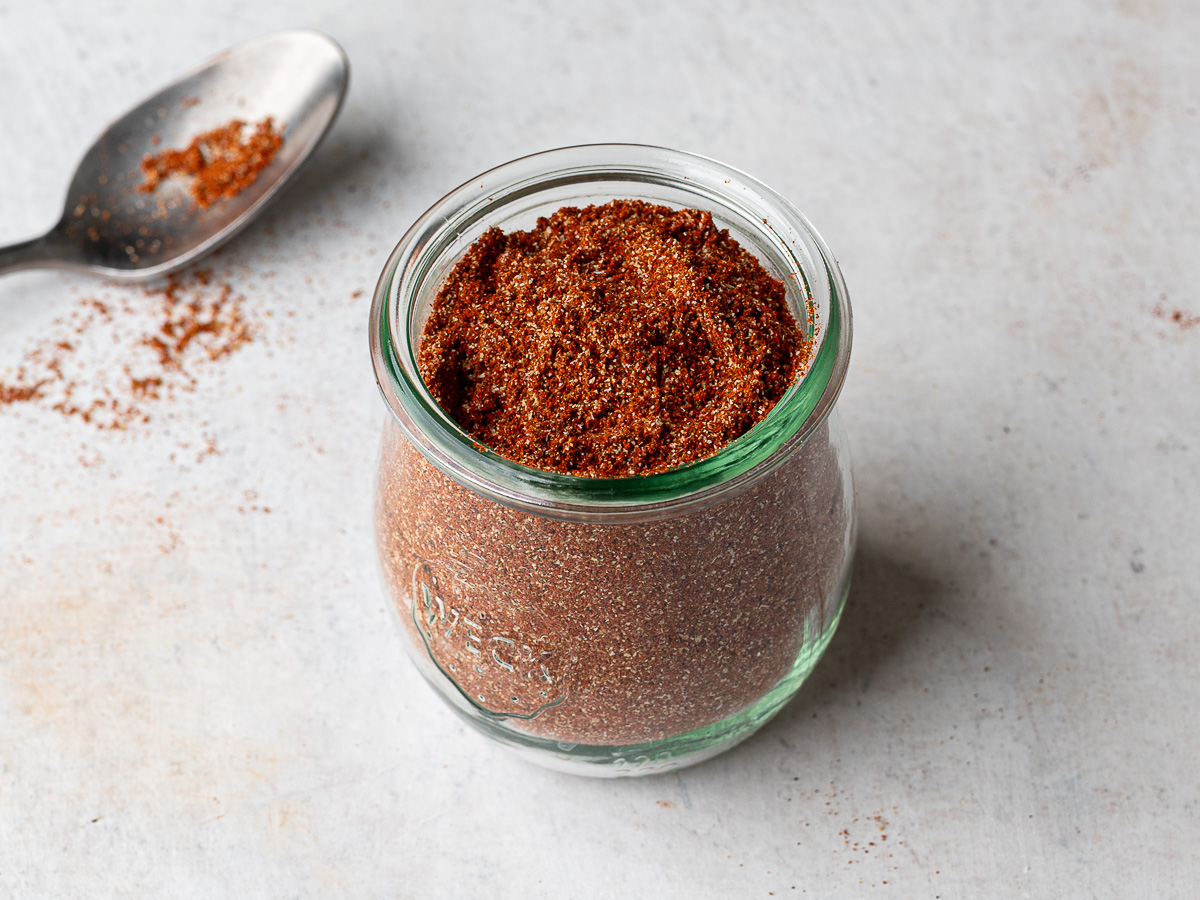 Homemade sazón seasoning in a glass Weck jar with spoon in the background. 