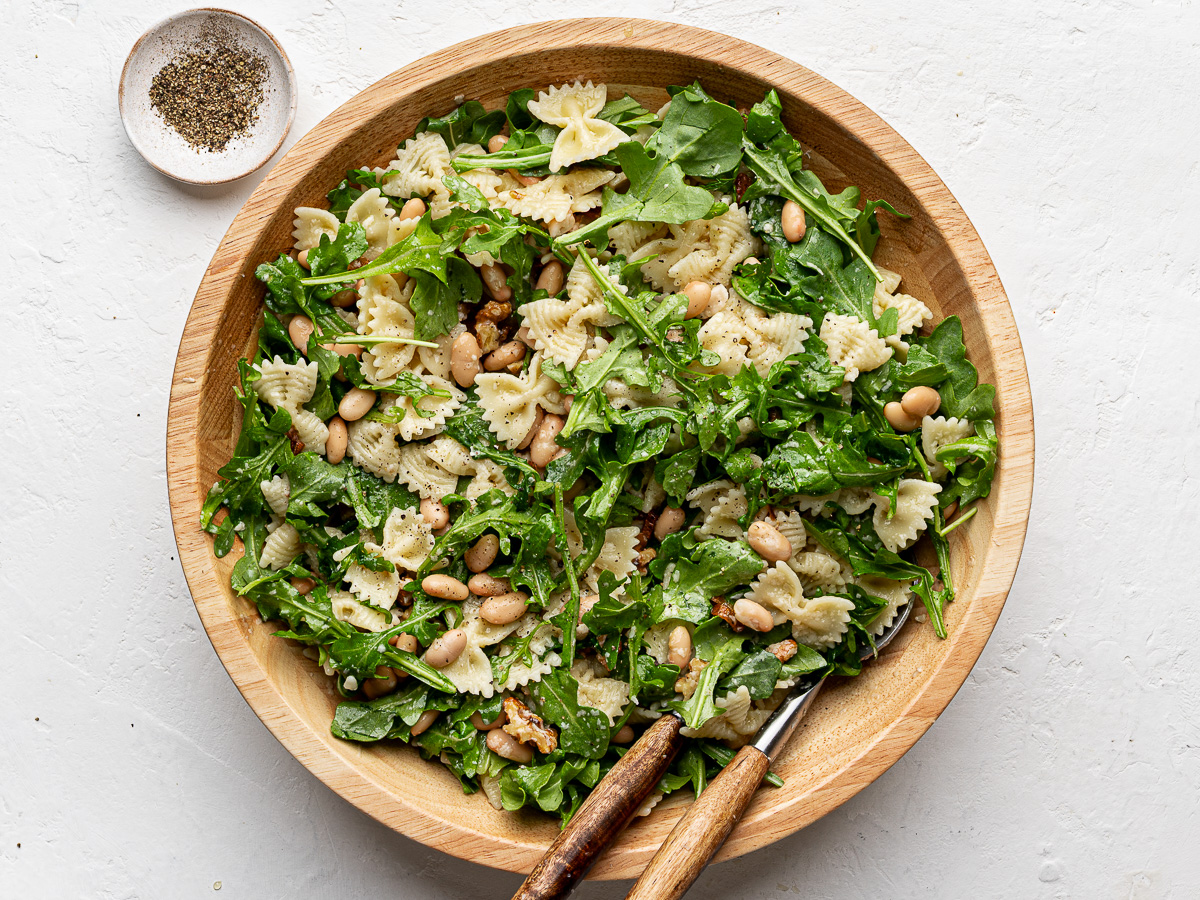 Pasta salad tossed with arugula in wood bowl. 