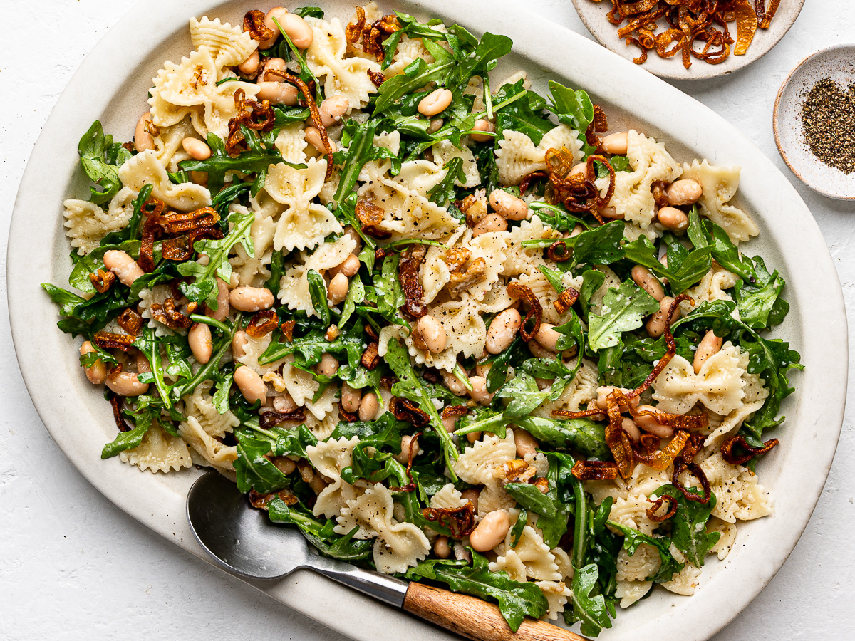 Close-up of arugula Pasta Salad with white beans and crispy shallots served on a large white platter.