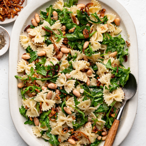 Arugula Pasta Salad with white beans and crispy shallots served on a large white platter.