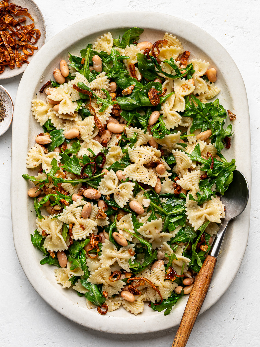 Arugula Pasta Salad with white beans and crispy shallots served on a large white platter.