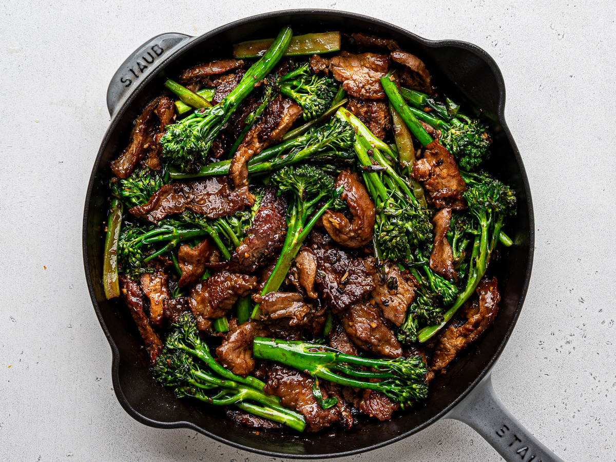 Beef and broccolini tossed with sauce in skillet. 