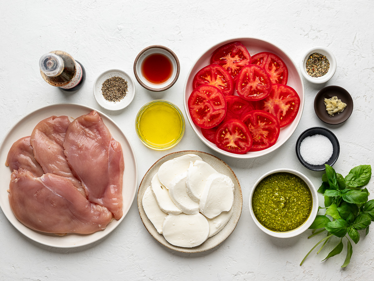 Ingredients laid out for making grilled Chicken Caprese with 4 chicken breasts, pesto, mozzarella, tomatoes, balsamic, and fresh basil.