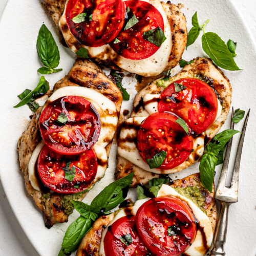 Assembled grilled Caprese chicken topped with tomatoes, fresh basil, olive oil, and balsamic drizzle.