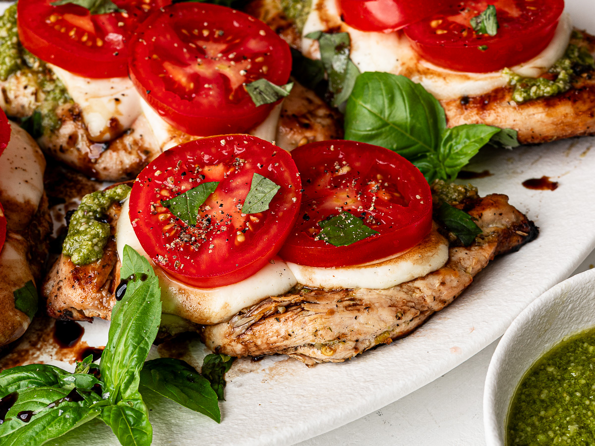 Close-up of Grilled Caprese chicken on a platter topped with tomato slices, fresh basil, and a drizzle of balsamic glaze.