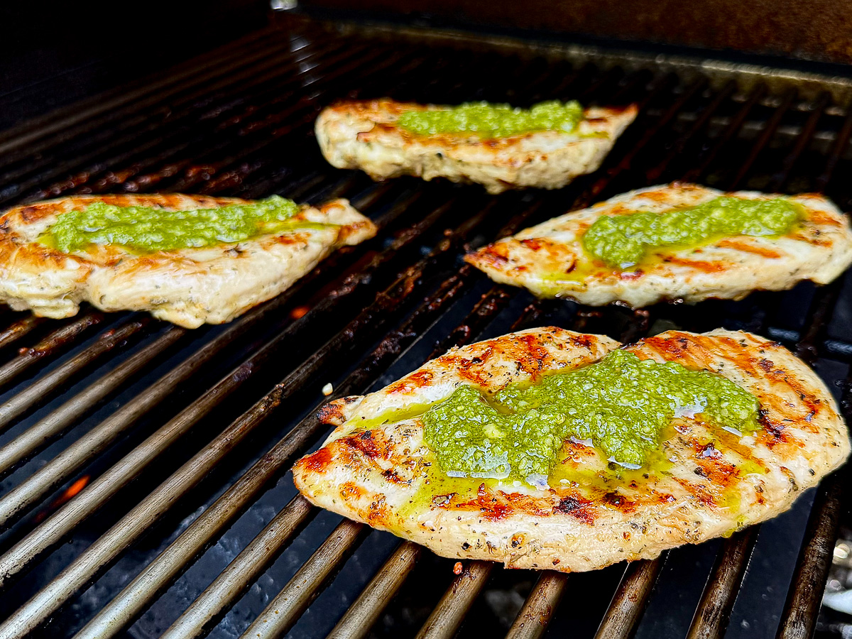 Chicken breasts on the grill topped with basil pesto.