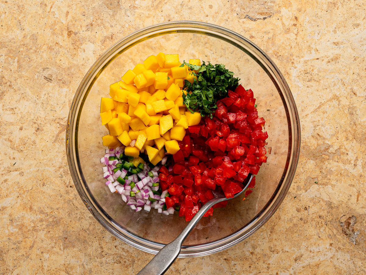 Diced mangoes, tomatoes and cilantro added to mixing bowl. 