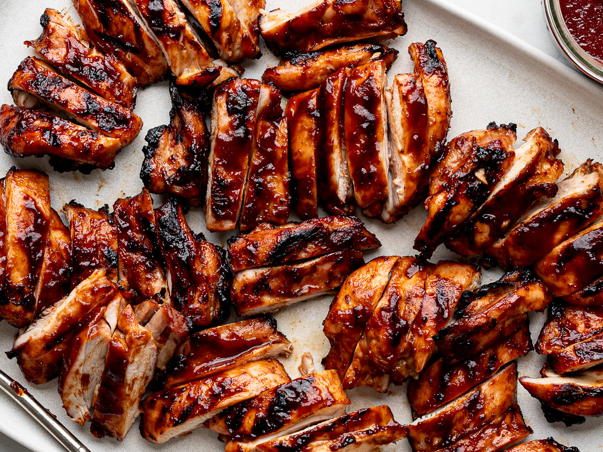 Close-up of sliced BBQ chicken thighs served on a white platter.