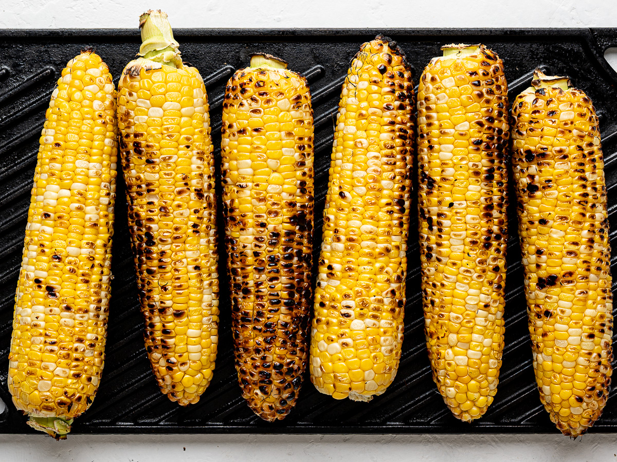 Six grilled ears of corn on a grill pan.