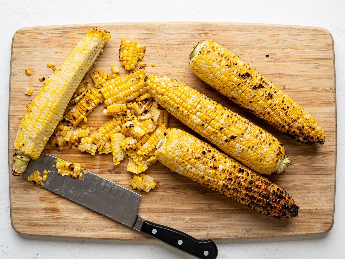 Cutting kernels off the cob on a cutting board.