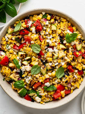 Close-up of rilled corn salad with grilled zucchini and grilled red peppers served in a beige bowl.