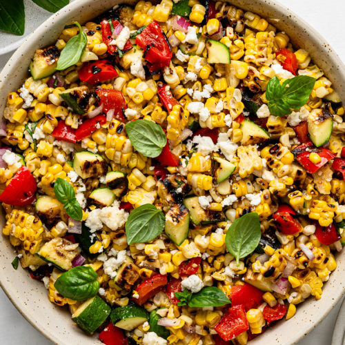 Close-up of rilled corn salad with grilled zucchini and grilled red peppers served in a beige bowl.