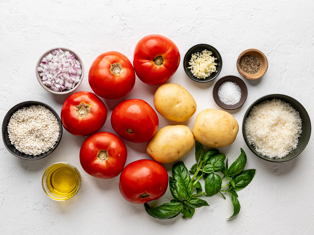 Ingredients for rice stuffed tomatoes including fresh tomatoes, potatoes, arborio rice, onion, garlic, and herbs.