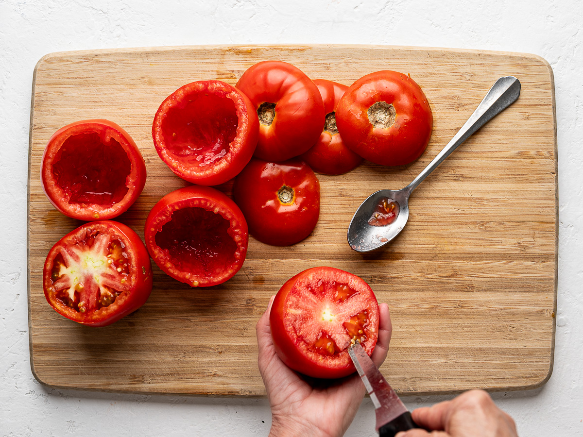 Ripe tomatoes being hollowed out with a small paring knife, ready for stuffing.