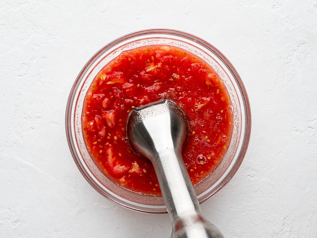 Tomato pulp in glass bowl about to be blended with immersion blender.
