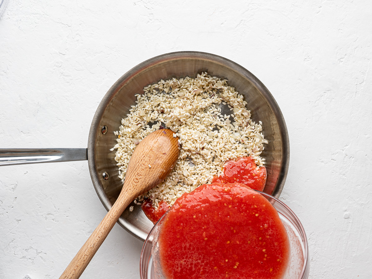 Pouring tomato pulp into skillet with pre-cooked rice mixture.