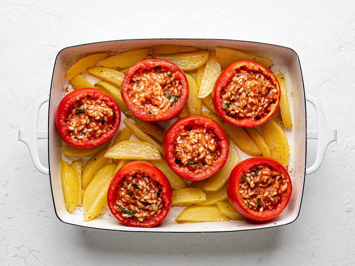 Tomatoes filled with savory rice mixture sitting atop potato wedges before baking.