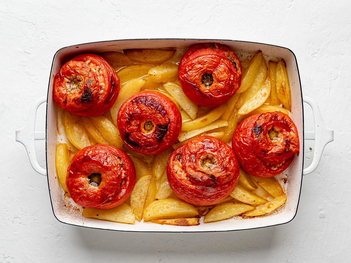 Baked rice stuffed tomatoes served over crispy roasted potato wedges in white baking dish.