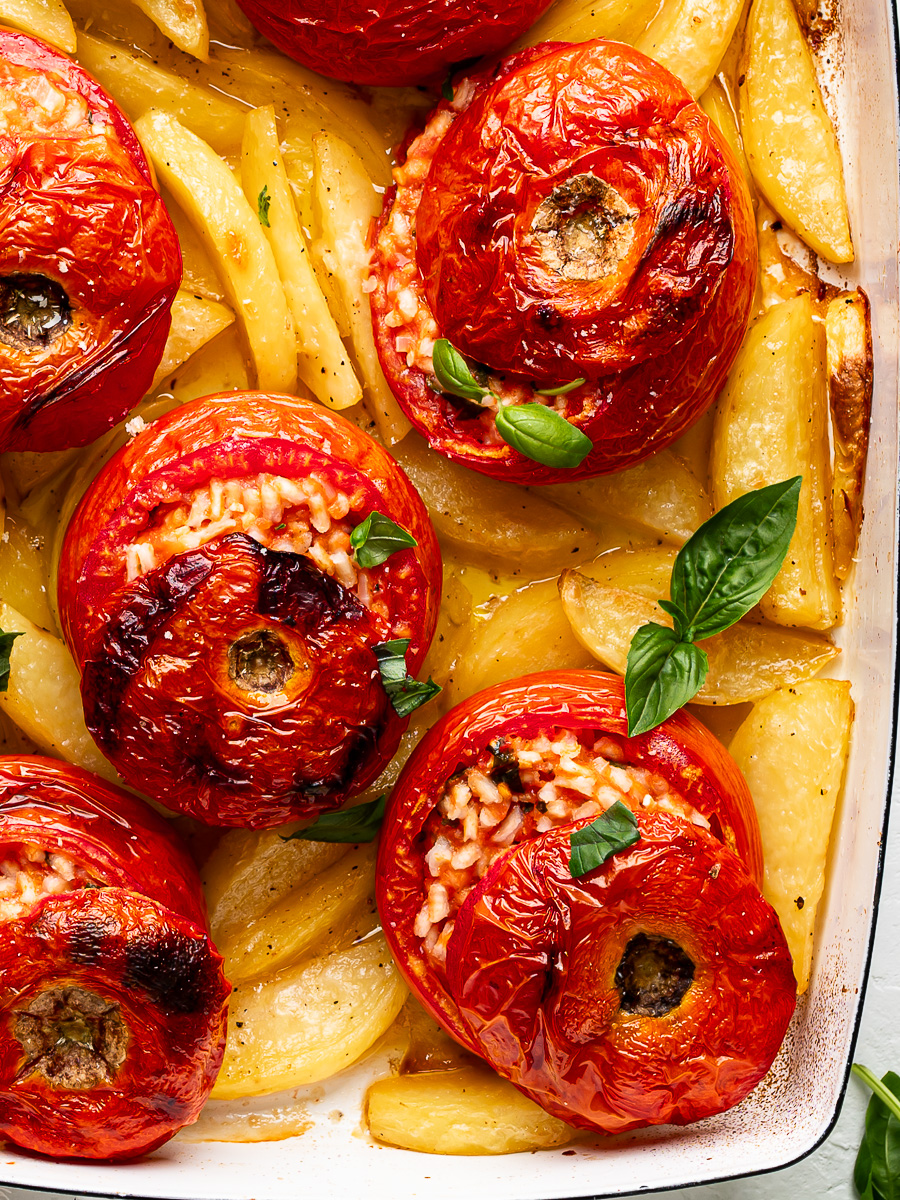 Close-up of baked rice stuffed tomatoes served over crispy roasted potato wedges garnished with basil leaves.