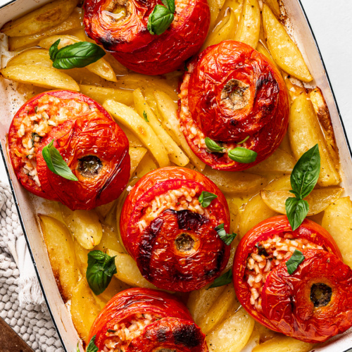 Golden baked rice stuffed tomatoes over crispy roasted potato wedges in baking dish garnished with fresh basil.
