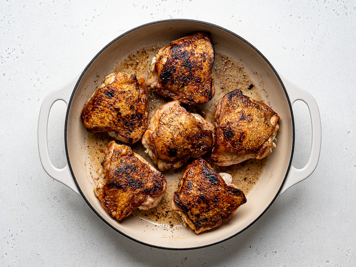 Six chicken thighs browning in skillet.