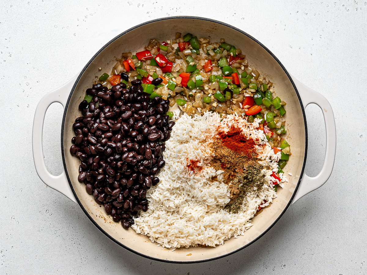 Rice, black beans and spices added to sautéed vegetables in skillet.