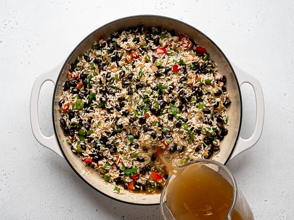 Pouring chicken broth into skillet with rice.