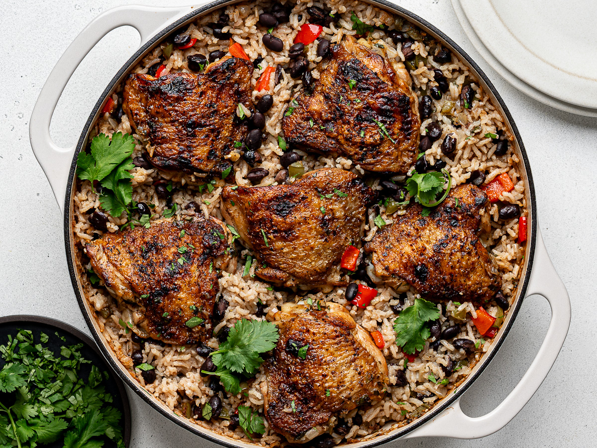 Baked chicken and rice with black beans in skillet, garnished with chopped cilantro leaves.