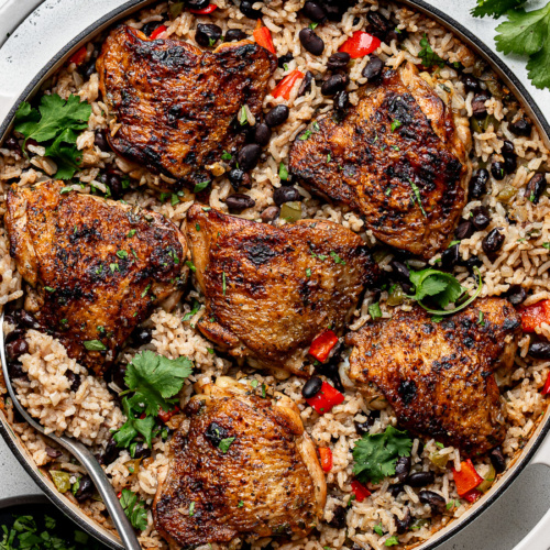 Baked dish of chicken with rice and black beans in white skillet.