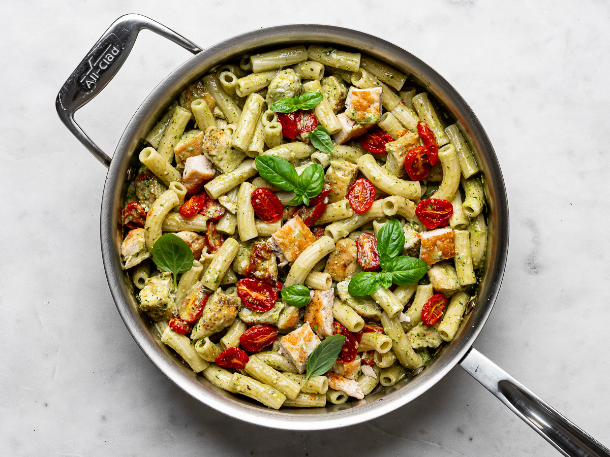 Finished creamy chicken pesto pasta in stainless steel skillet with roasted cherry tomatoes.