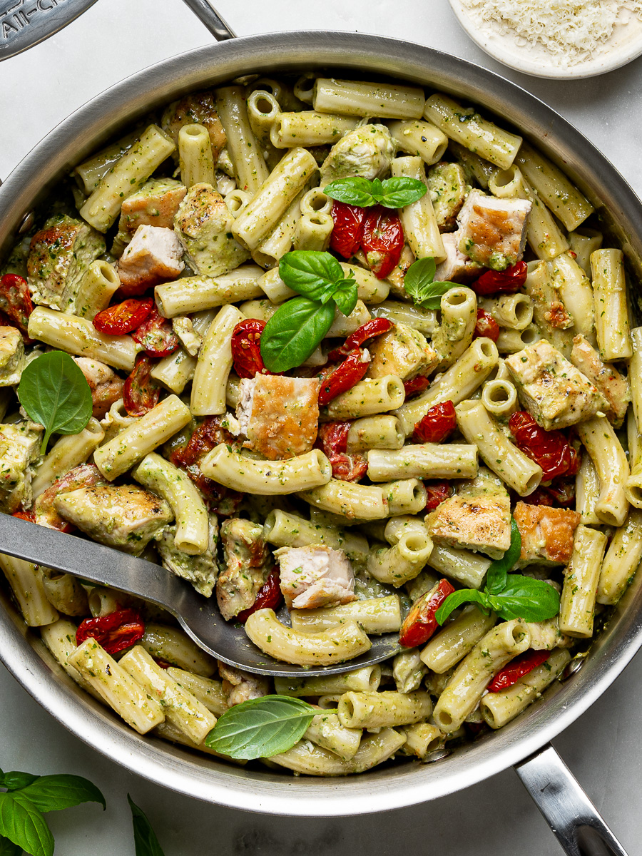 Close-up of finished creamy chicken pesto pasta in stainless steel skillet with roasted cherry tomatoes.