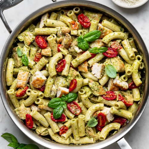 Close-up of finished creamy chicken pesto pasta in stainless steel skillet with roasted cherry tomatoes.