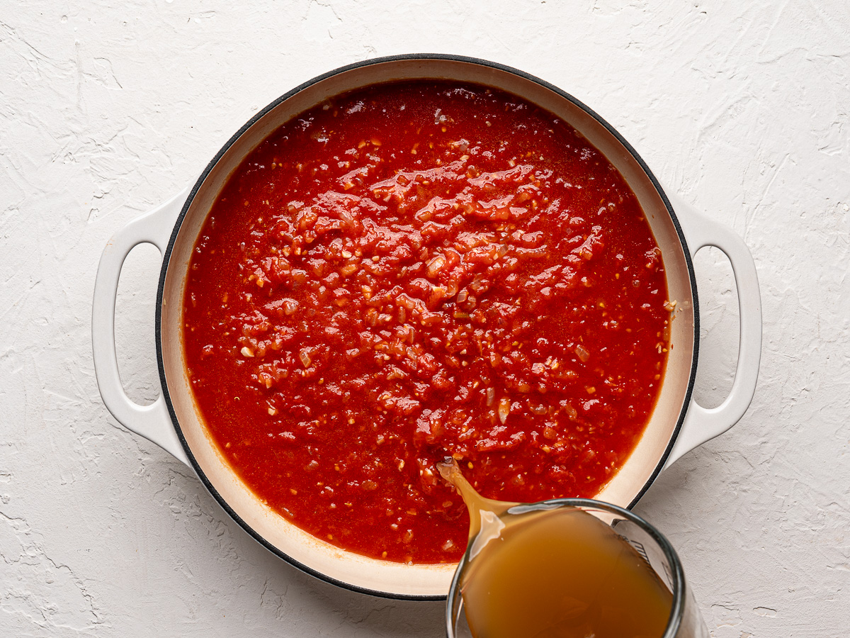Pouring broth into tomato sauce in skillet.