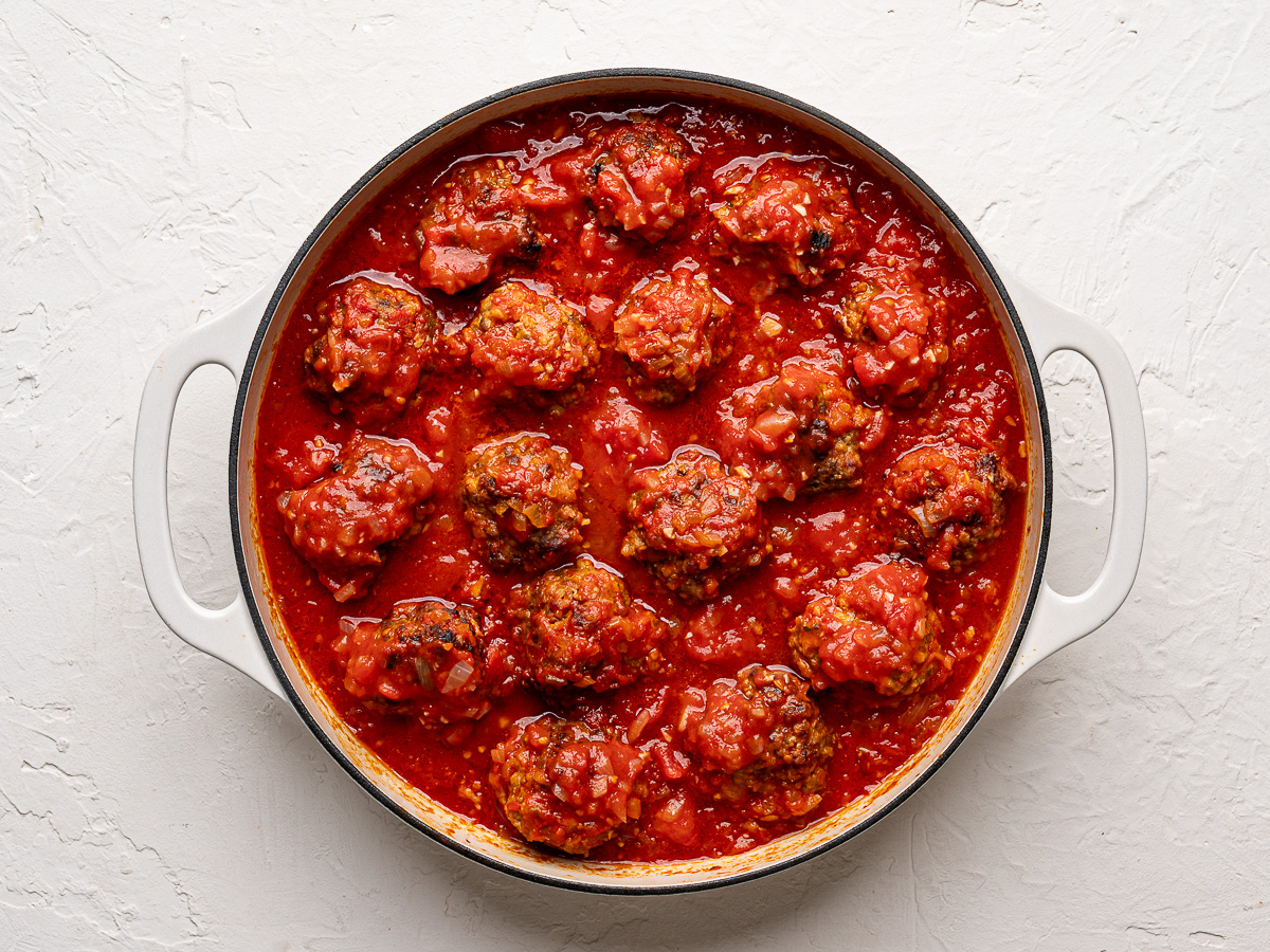 Meatballs braised in tomato sauce in skillet.