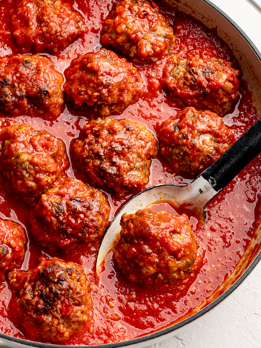 Closeup of tender ricotta meatballs in large white skillet with large serving spoon.