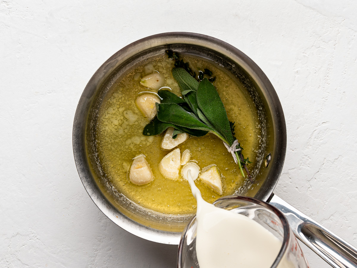 Pouring cream into butter and garlic mixture in saucepan.