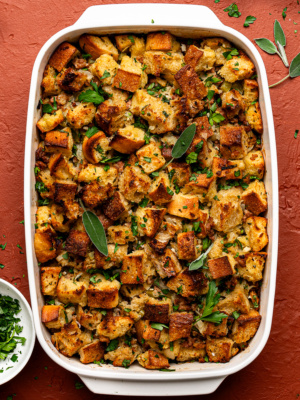 Baked sausage and sage stuffing in a white baking dish, garnished with fresh herbs.