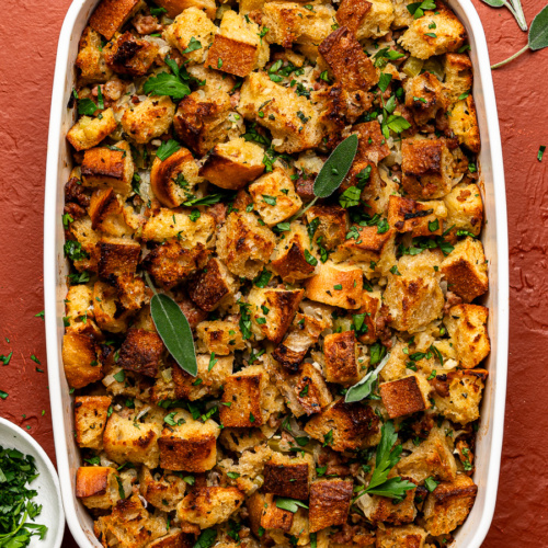 Baked sausage and sage stuffing in a white baking dish, garnished with fresh herbs.