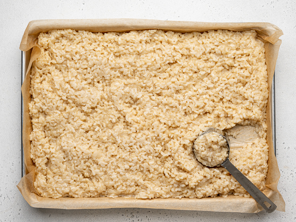 Using a 1/4 cup measuring cup to scoop out cooked rice to shape balls.