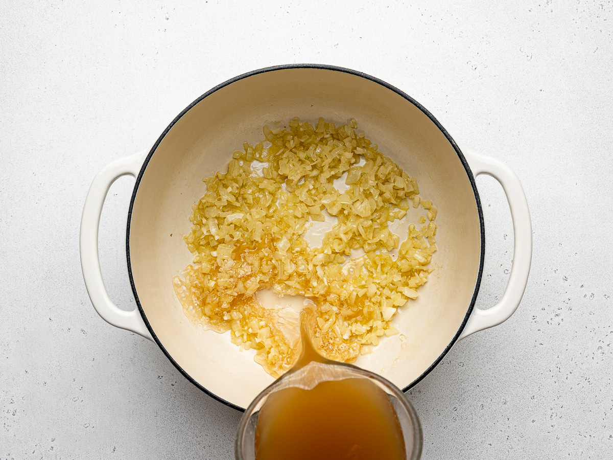 Pouring chicken broth over sautéed arborio rice in dutch oven.