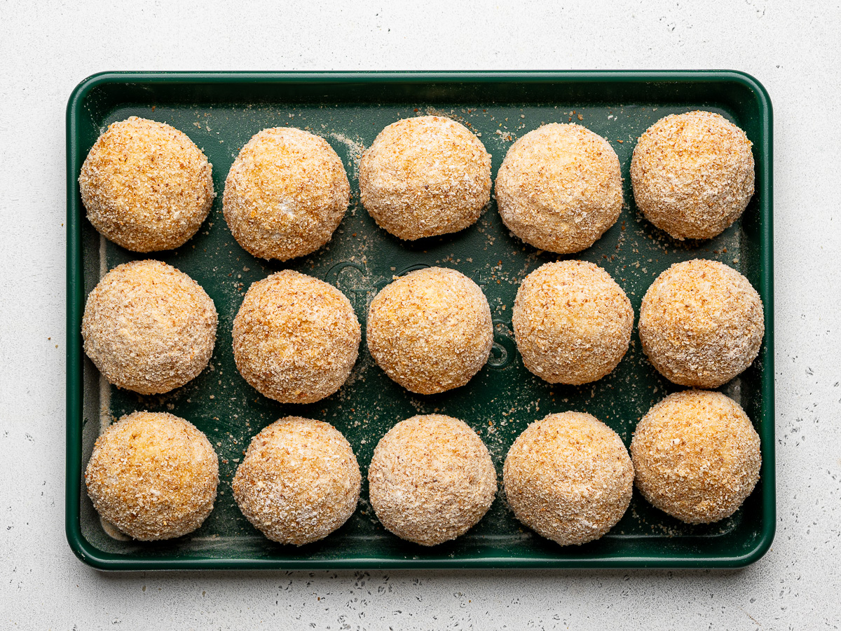 All of the bread-coated rice balls on a green sheet pan.