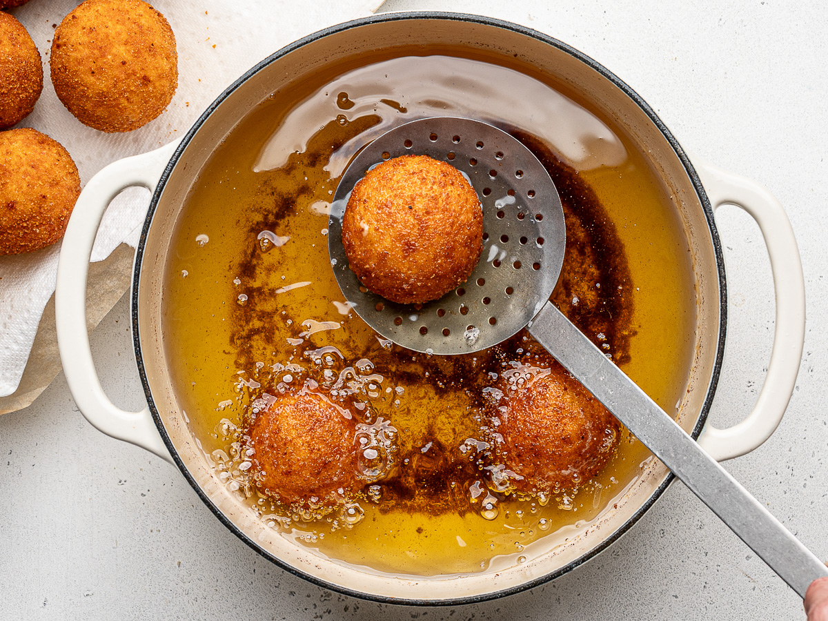 Scooping rice ball frying in oil with slotted spoon.
