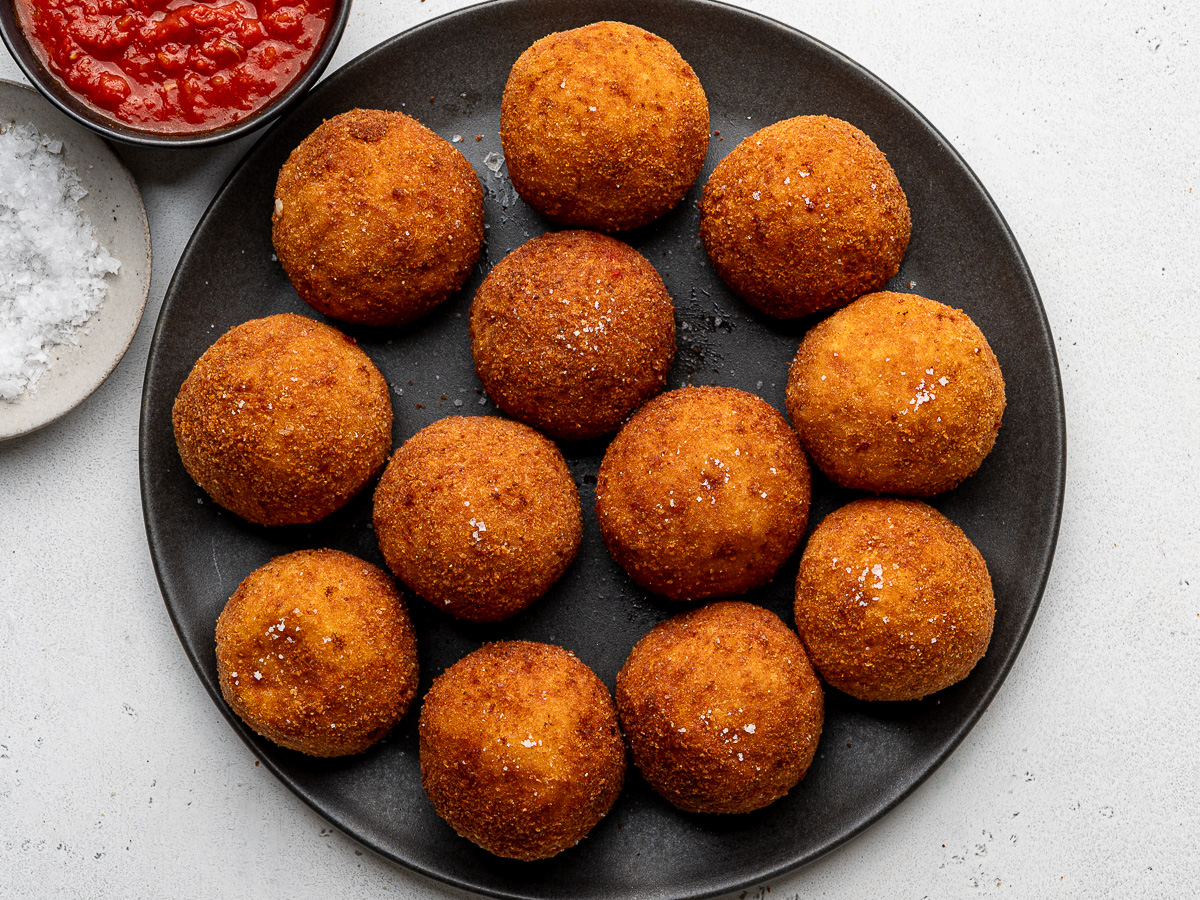 Fried rice balls on black serving platter sprinkled with flaky salt.